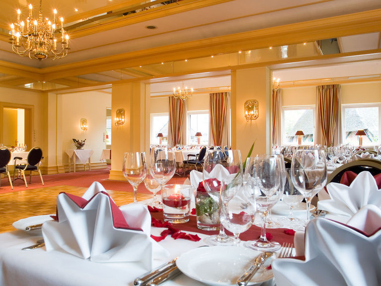 Ein Saal eingedeckt für eine große Feier, im Vordergrund sehen Sie einen reich gedeckten Tisch.